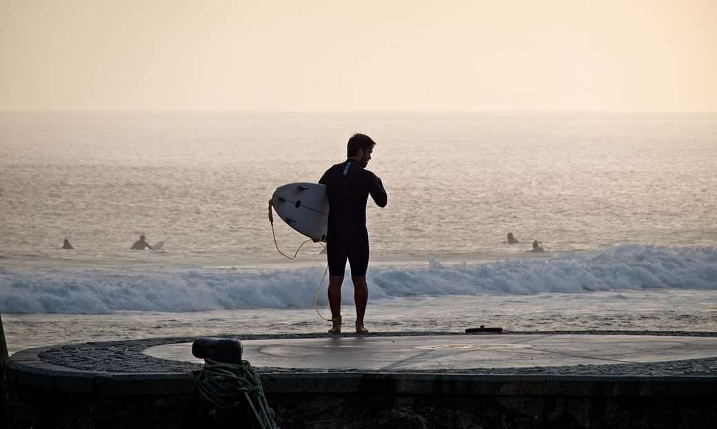 man holding surfboard near seashore jigsaw puzzle online
