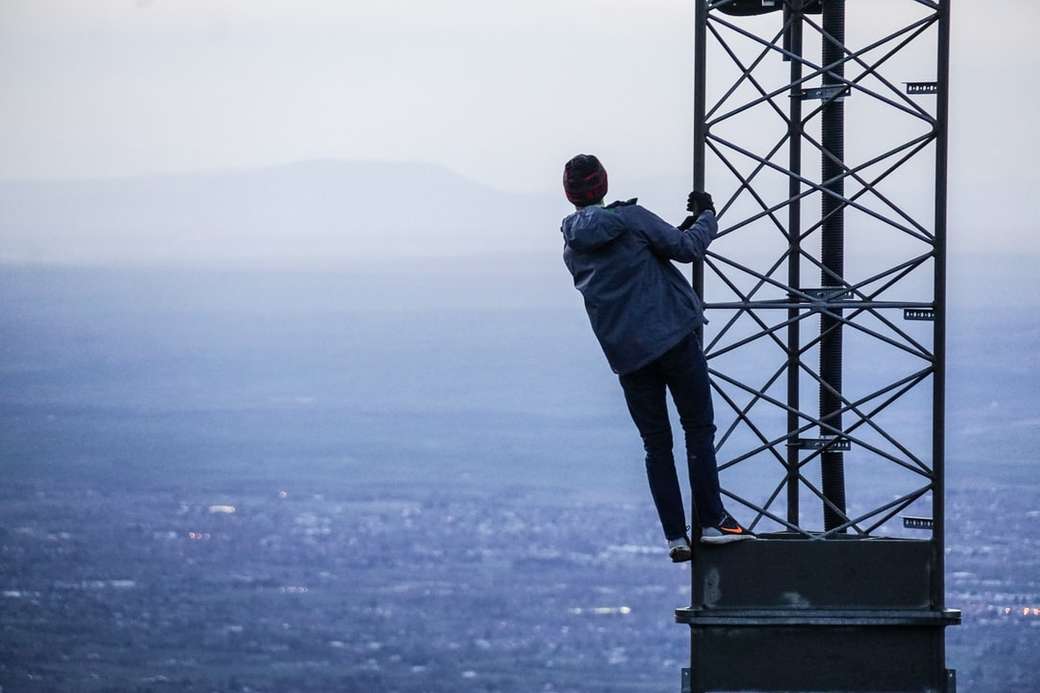 Mann, der tagsüber auf Turm nahe Gebäuden klettert Online-Puzzle