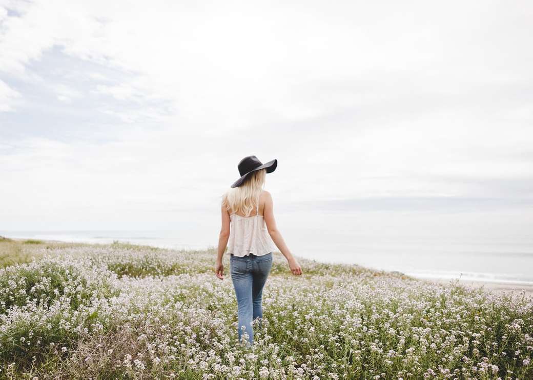 žena nosí černý klobouk chůzi přes květinové pole během dne online puzzle