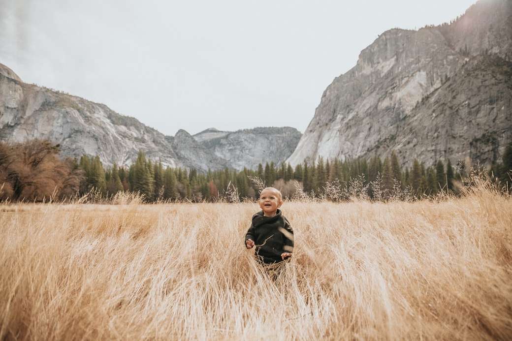 garoto de jaqueta preta fica na grama marrom perto da montanha quebra-cabeças online
