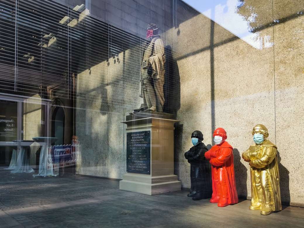3 Männer im roten Gewand stehen tagsüber in der Nähe der Statue Puzzlespiel online