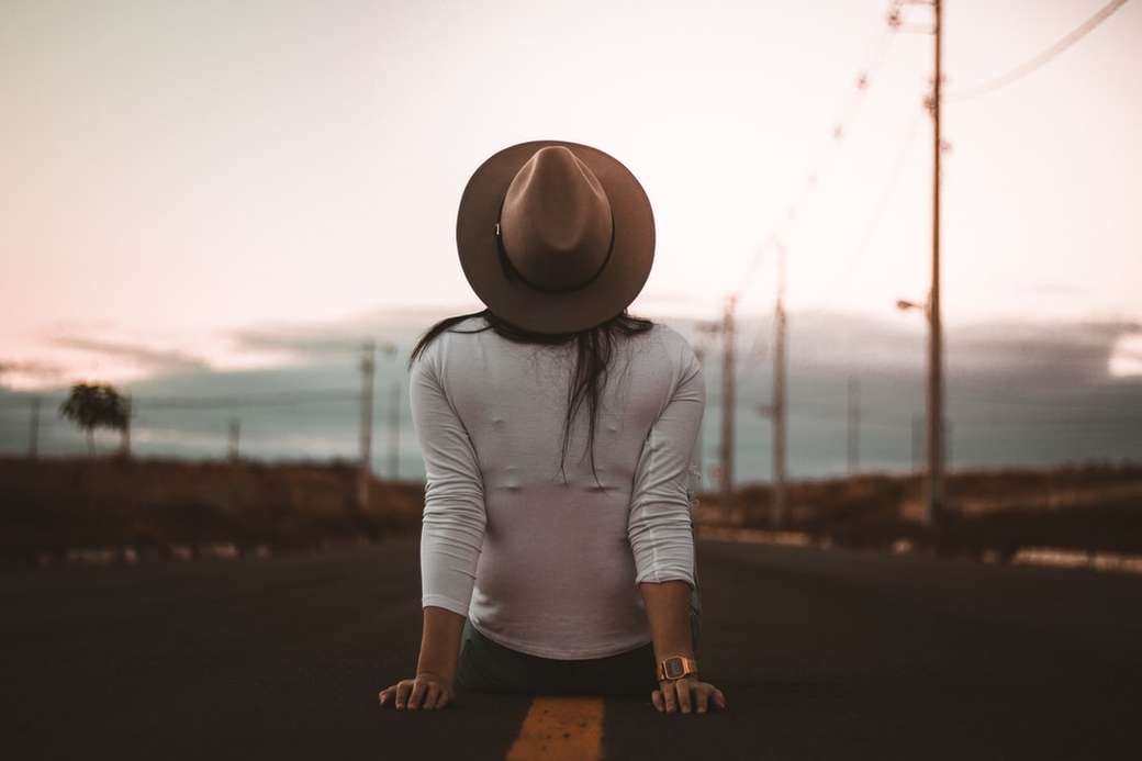 жінка сидить на дорозі в білій сорочці та коричневому капелюсі онлайн пазл