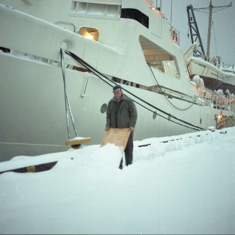 άντρας στέκεται στο χιόνι κοντά σε βάρκα κατά τη διάρκεια της ημέρας παζλ online