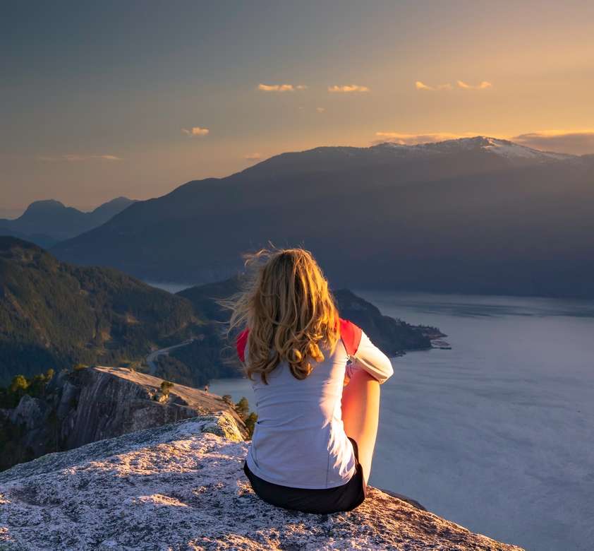 Frau, die oben auf Berg bei Sonnenuntergang sitzt. Puzzlespiel online