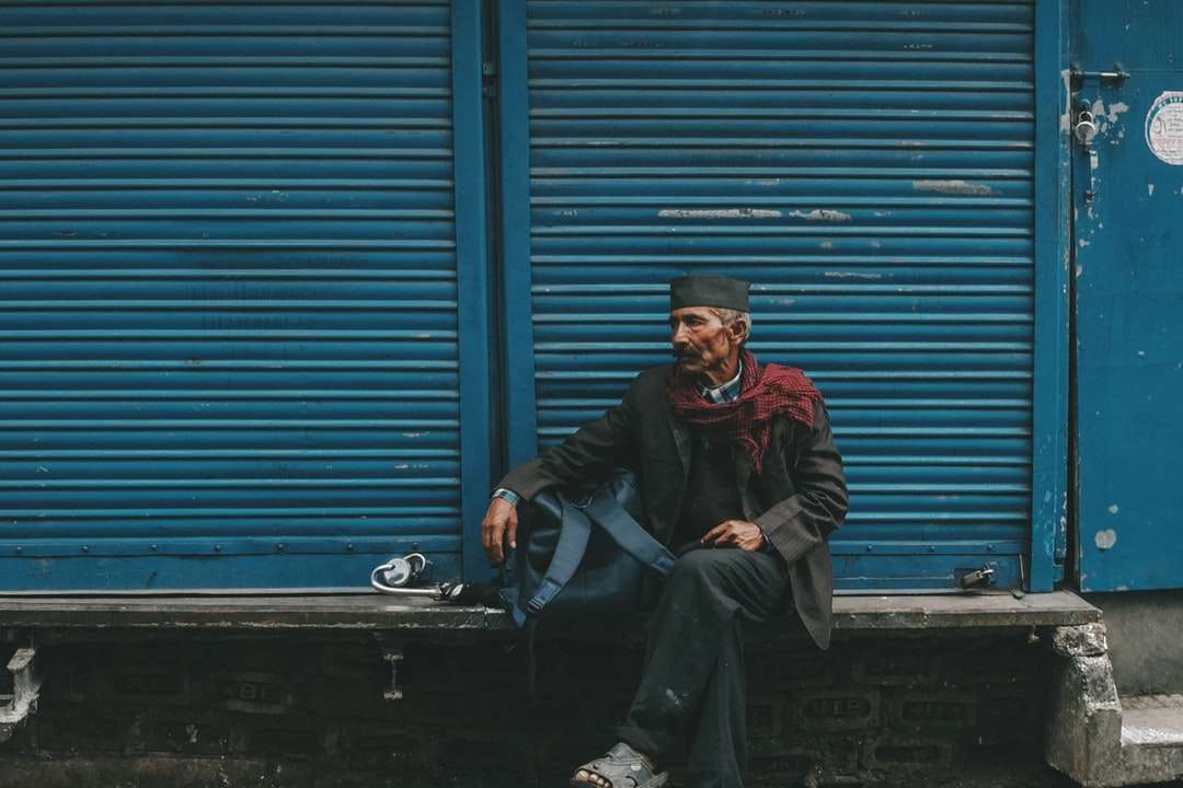 bărbat așezat pe o bancă gri, în fața ușii oblon albastre puzzle online