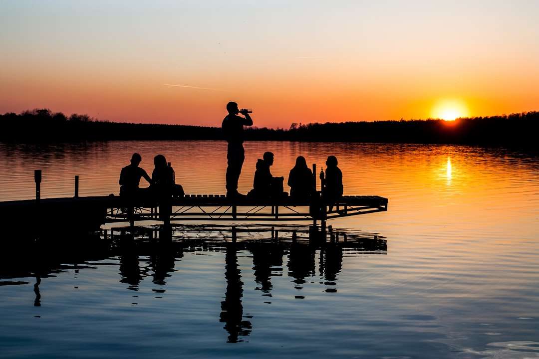 Gruppe von Menschen auf Holzdock während des Sonnenuntergangs Online-Puzzle