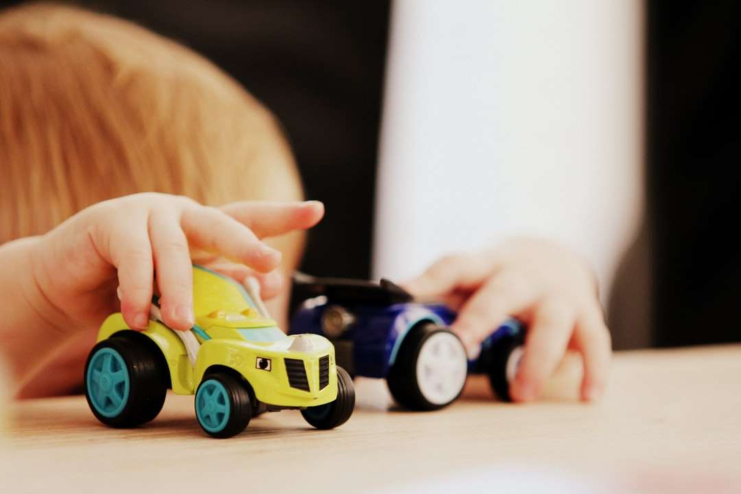 Kind spielt mit zwei verschiedenfarbigen Auto-Plastikspielzeugen Online-Puzzle