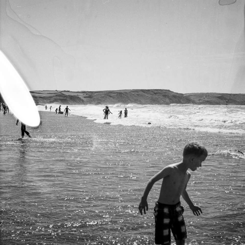 gråskalefoto av pojke som håller surfbrädan på stranden pussel på nätet