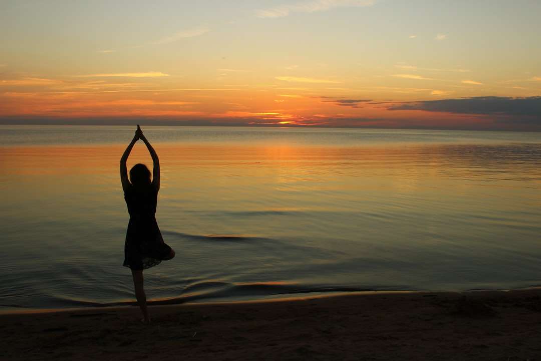 Mujer haciendo yoga cerca del cuerpo de agua tranquila durante la hora dorada rompecabezas en línea