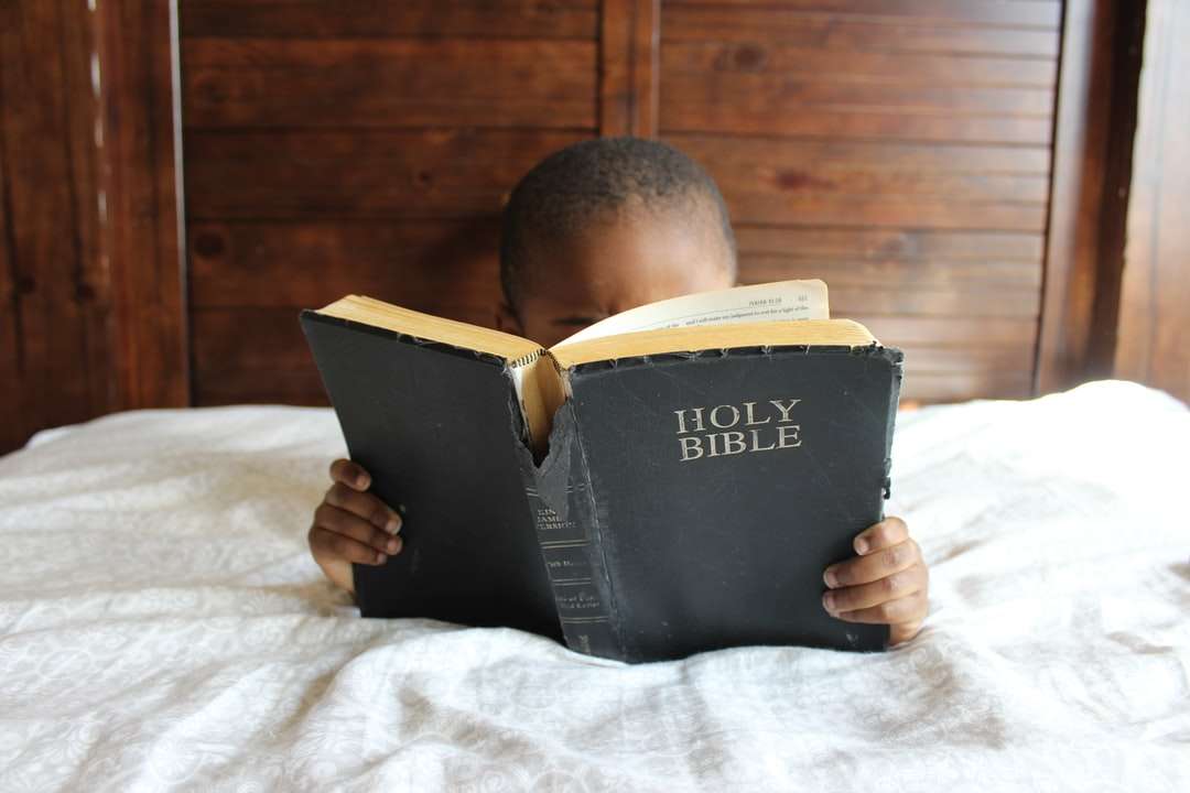 Niño leyendo la Santa Biblia mientras está acostado en la cama rompecabezas en línea