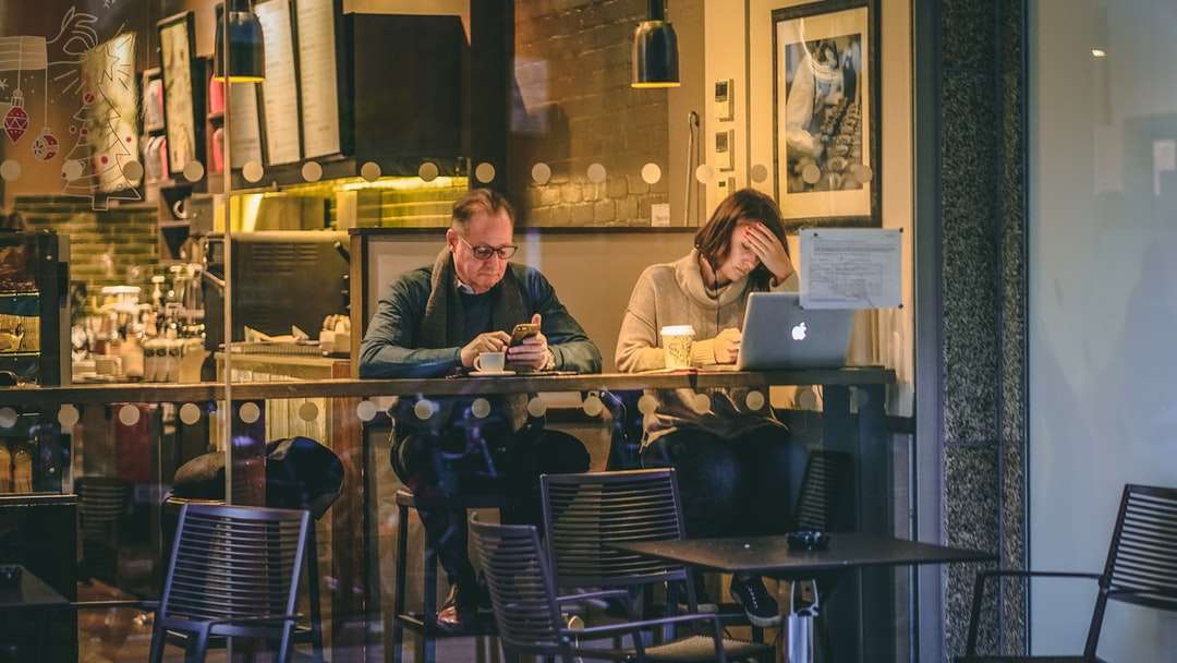 man met smartphone zit naast vrouw vooraan legpuzzel online