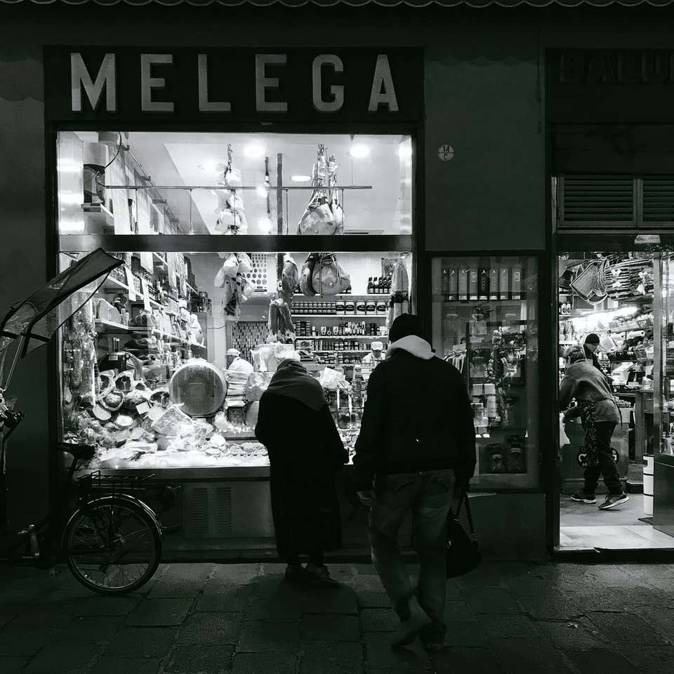 Foto en escala de grises de dos personas de pie en la tienda Melega rompecabezas en línea