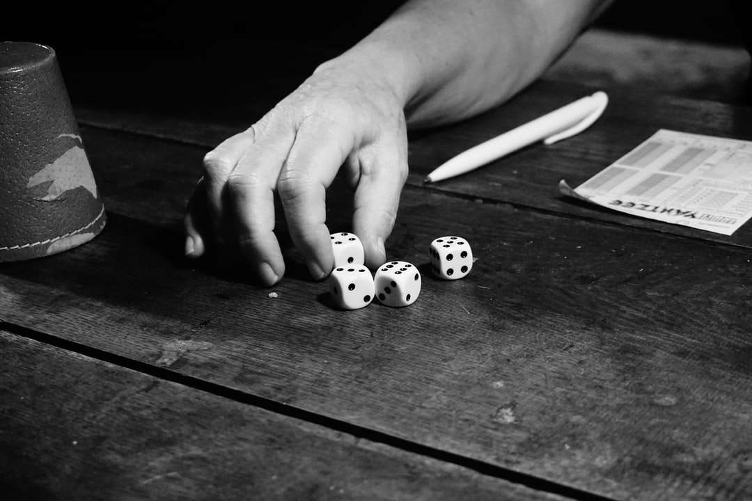 fotografia in scala di grigi di una persona che gioca con i dadi puzzle online