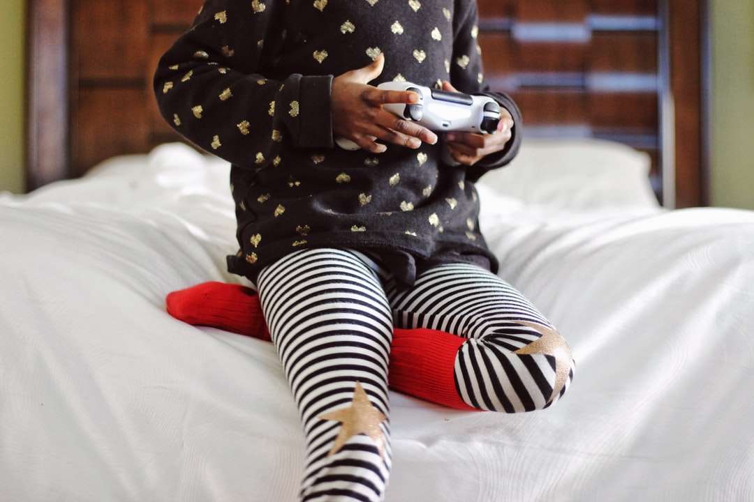 白いベッドに座っている灰色のゲームコントローラーを保持している子供たち ジグソーパズルオンライン