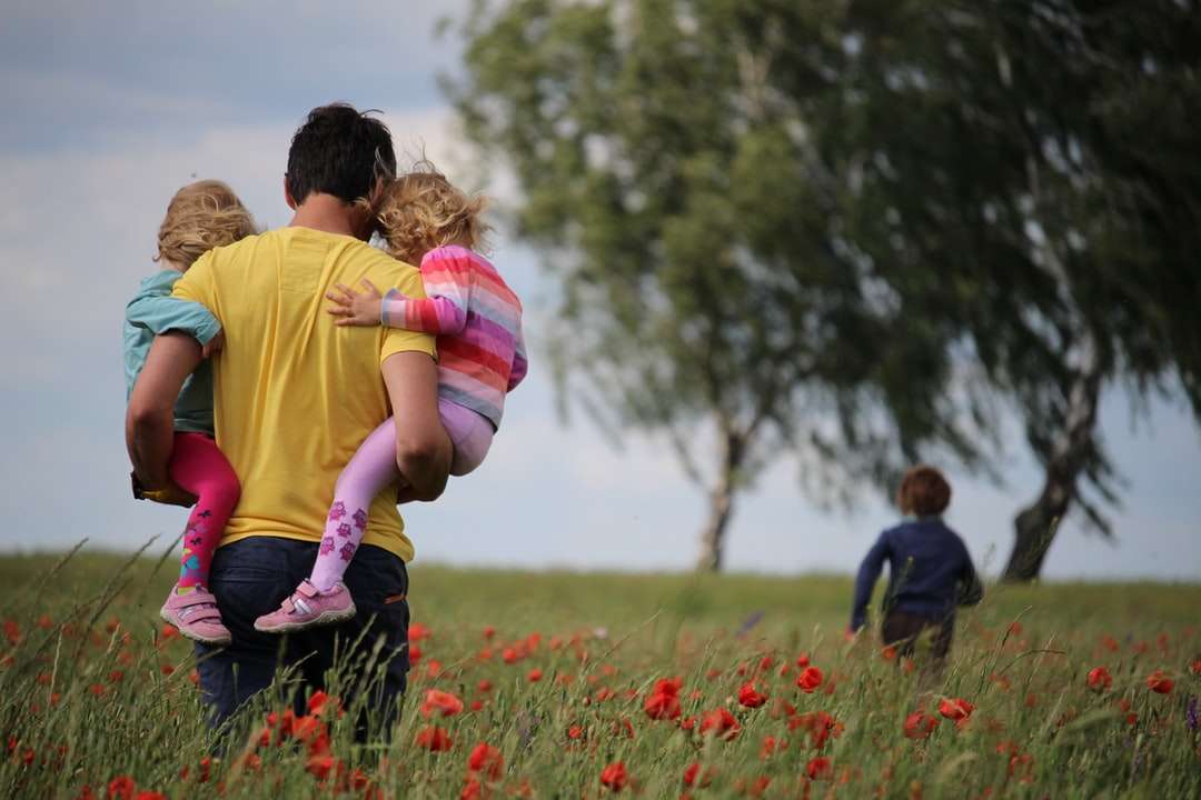 El hombre lleva a las niñas en el campo de flores de pétalos rojos rompecabezas en línea
