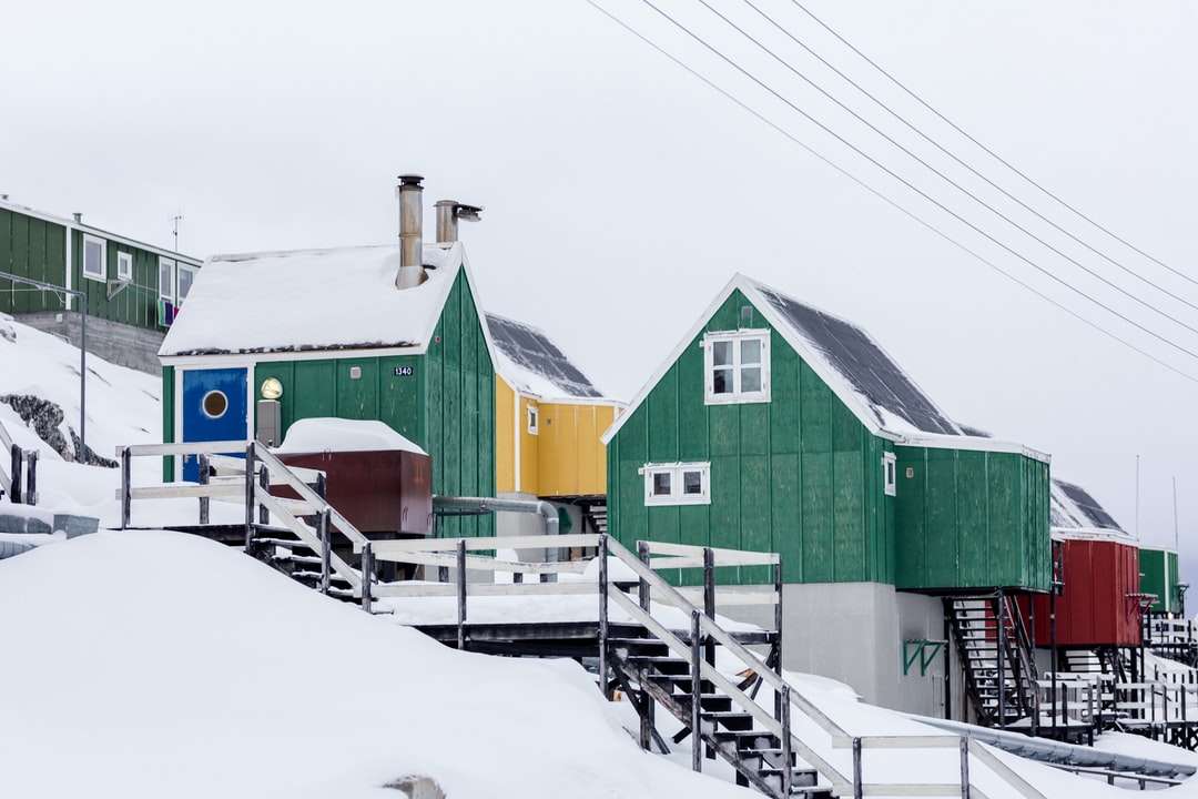 groene houten huizen op met sneeuw bedekte helling onder witte luchten online puzzel