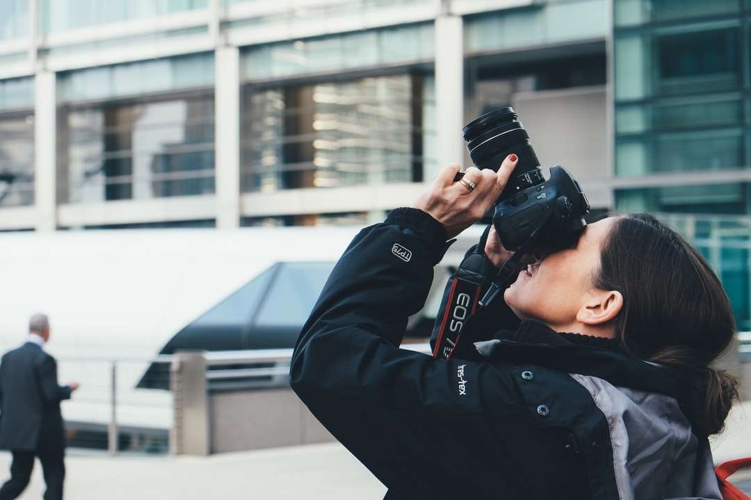 donna che indossa giacca grigia e nera utilizzando la fotocamera DSLR puzzle online