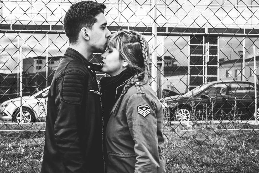 grijswaardenfoto van man kussen voorhoofd van vrouw in de buurt van hek legpuzzel online