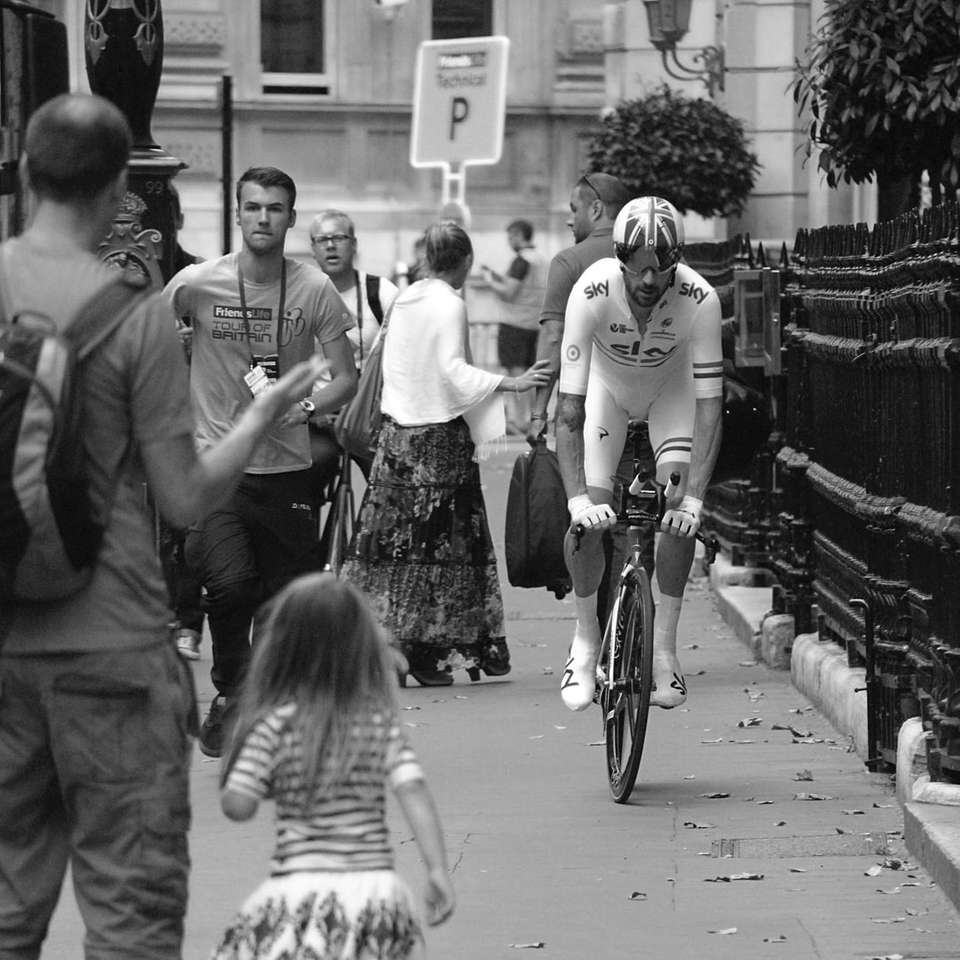 Foto en escala de grises del hombre en bicicleta junto a un grupo de personas rompecabezas en línea