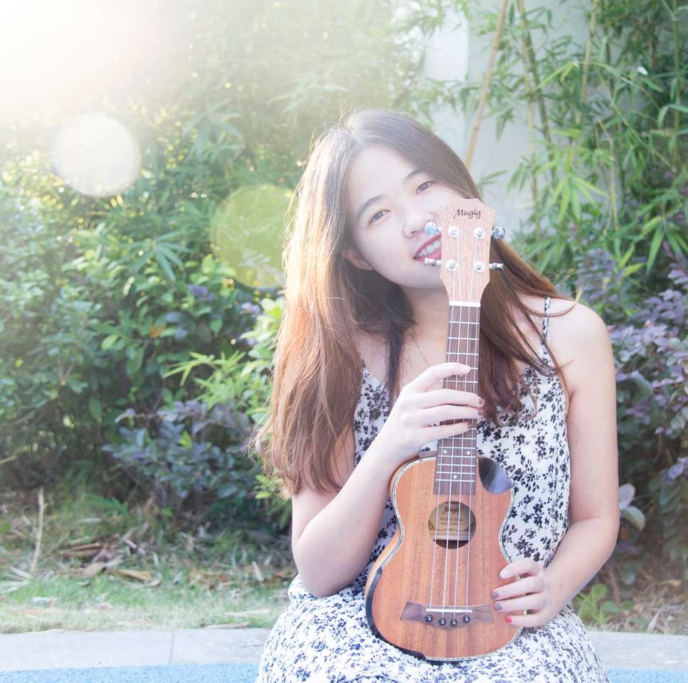 mulher sorridente segurando um ukulele perto de plantas verdes puzzle online