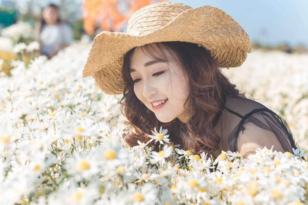 γυναίκα με καφέ ήλιο καπέλο στέκεται δίπλα σε λευκά λουλούδια online παζλ