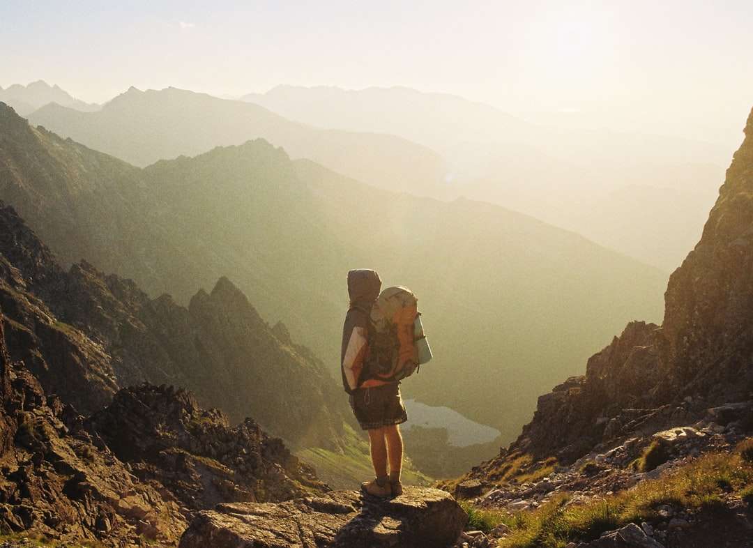 алпинист, стоящ на скала в близост с изглед към планината онлайн пъзел