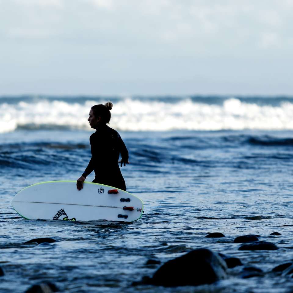 Frau, die weißes Surfbrett auf Gewässer hält Online-Puzzle