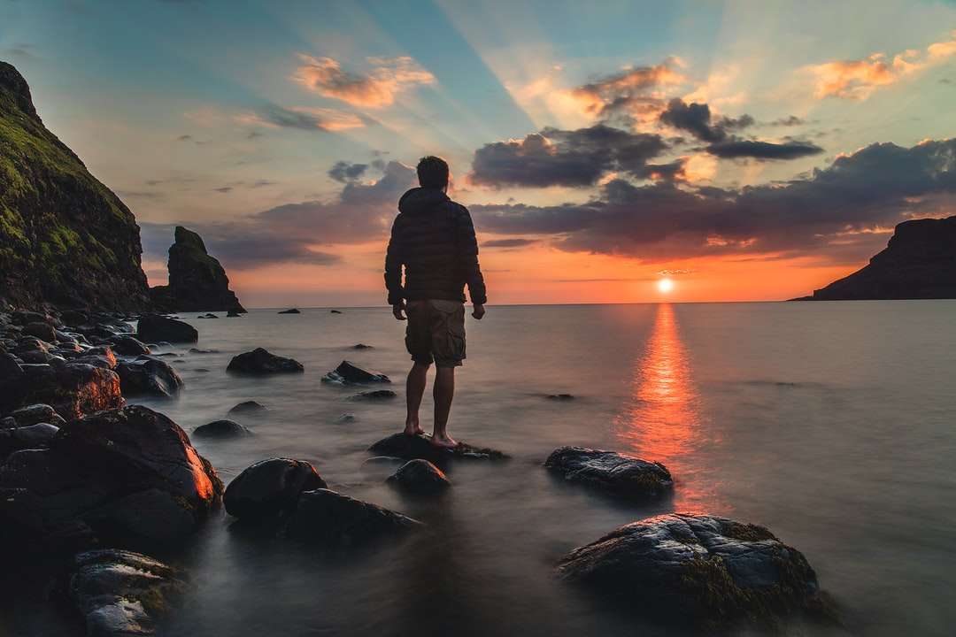 Mann, der auf Stein steht und Sonnenuntergang betrachtet Puzzlespiel online