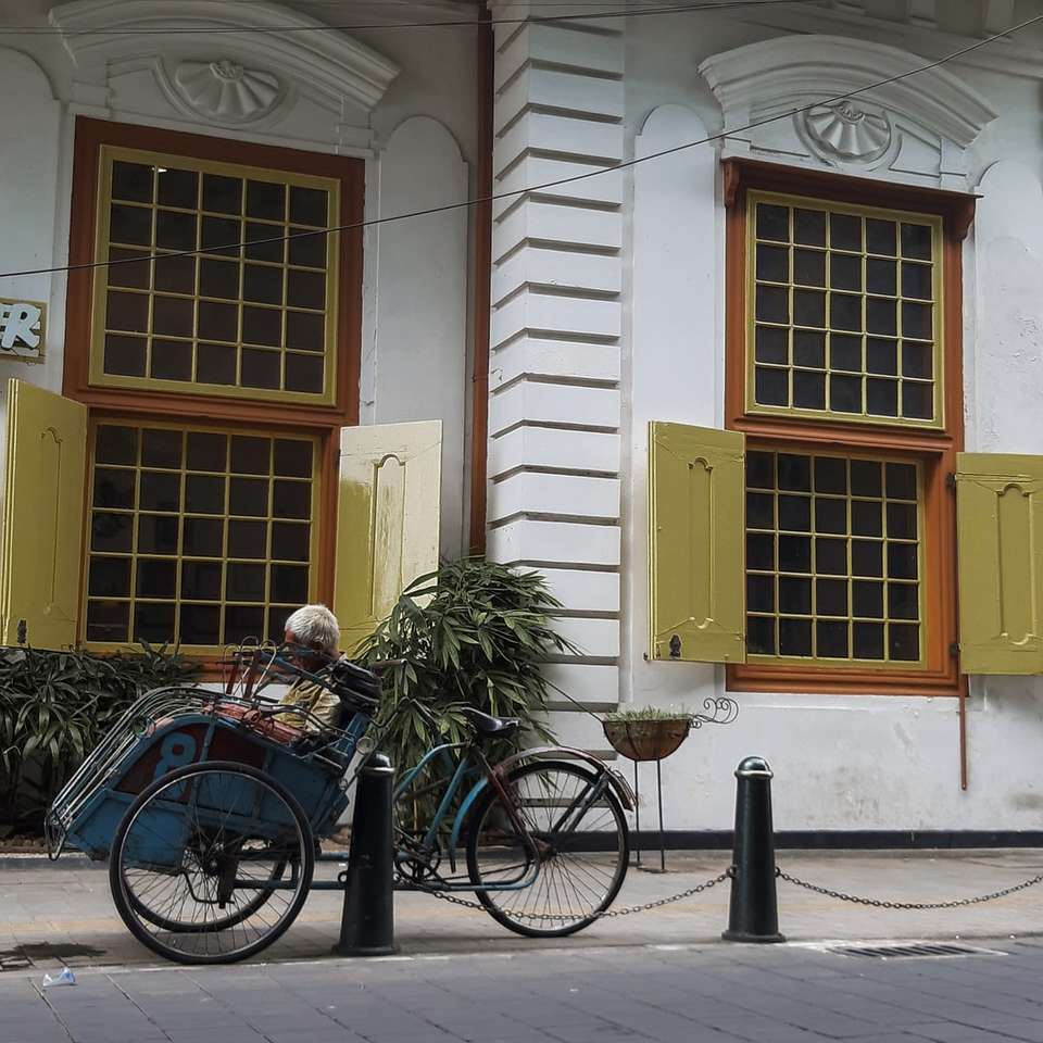 Vélo de ville bleu garé à côté du bâtiment en béton blanc et brun puzzle en ligne