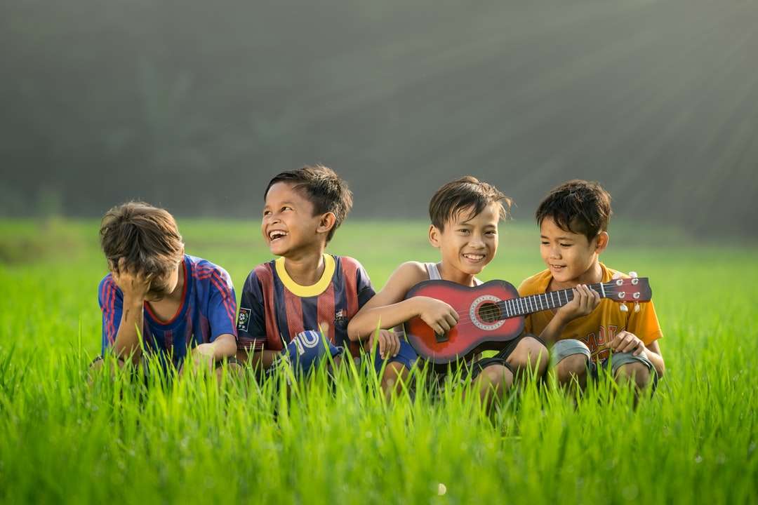 fyra pojkar skrattar och sitter på gräset under dagtid pussel på nätet