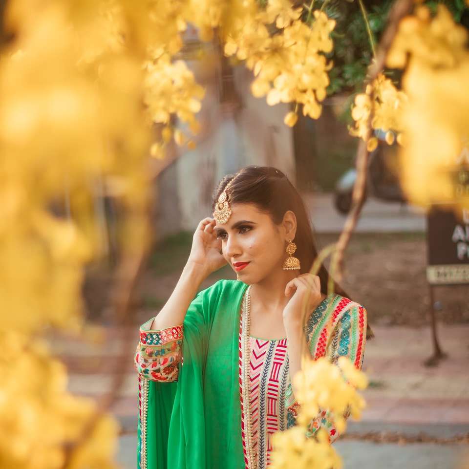 mujer en sari rojo y blanco de pie cerca de flores amarillas rompecabezas en línea
