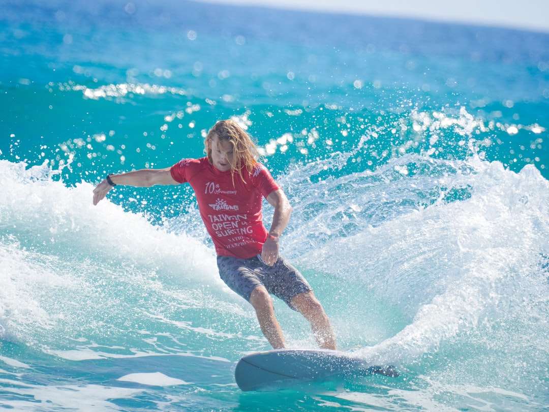 Chica en camiseta roja y pantalones cortos azules surfeando en el agua rompecabezas en línea