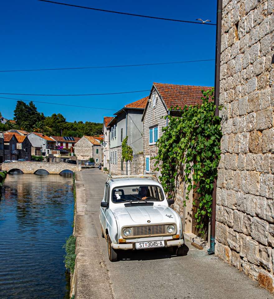 weißes Auto geparkt neben brauner Backsteinmauer in der Nähe von Gewässern Online-Puzzle