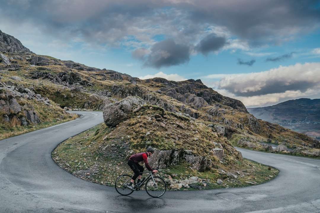 uomo in giacca rossa in bicicletta sulla strada vicino alla montagna puzzle online
