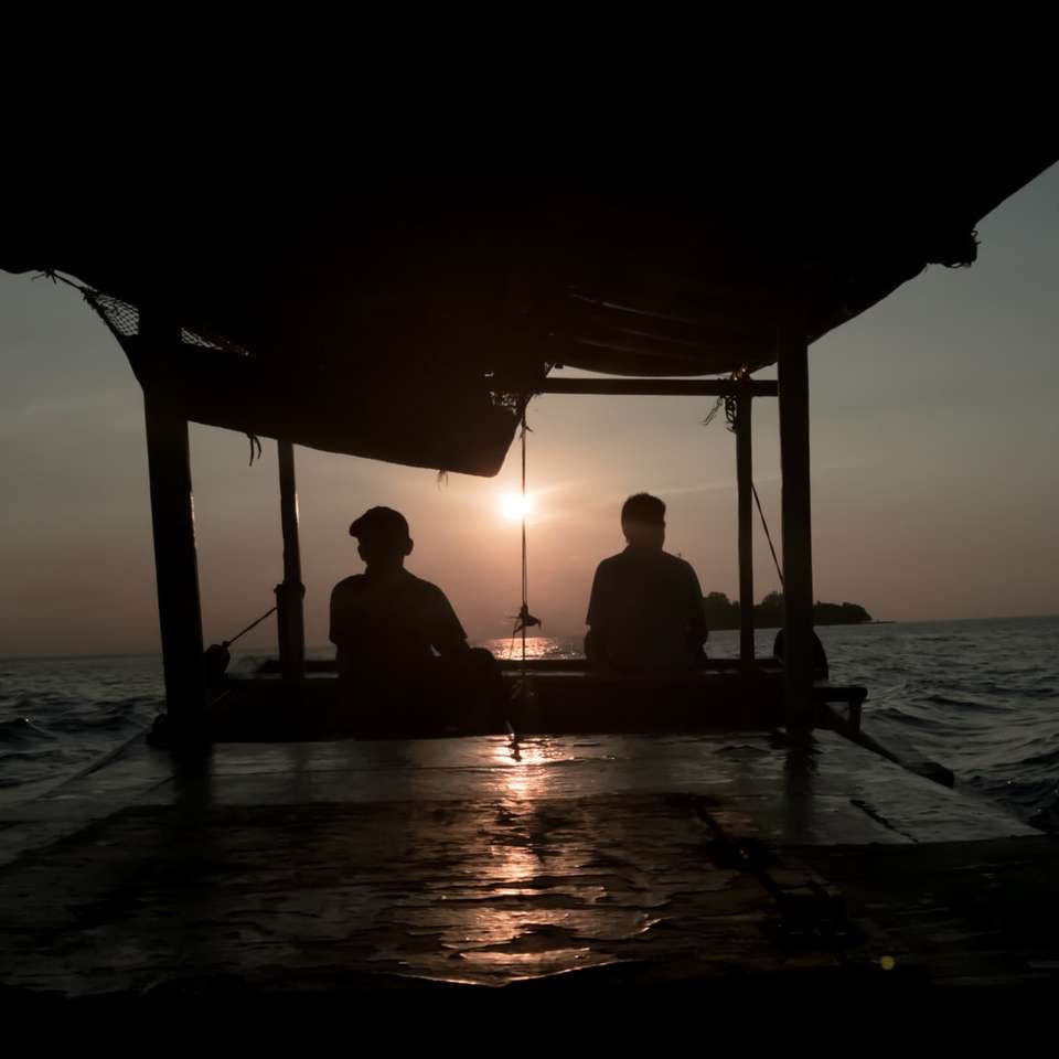 duas silhuetas de uma pessoa sentada perto do oceano à noite quebra-cabeças online