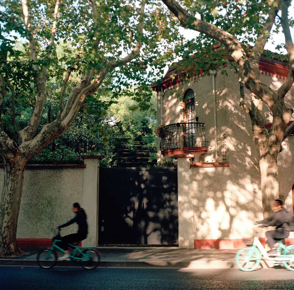 Mann im roten Hemd, das Fahrrad nahe grünen Bäumen reitet Puzzlespiel online