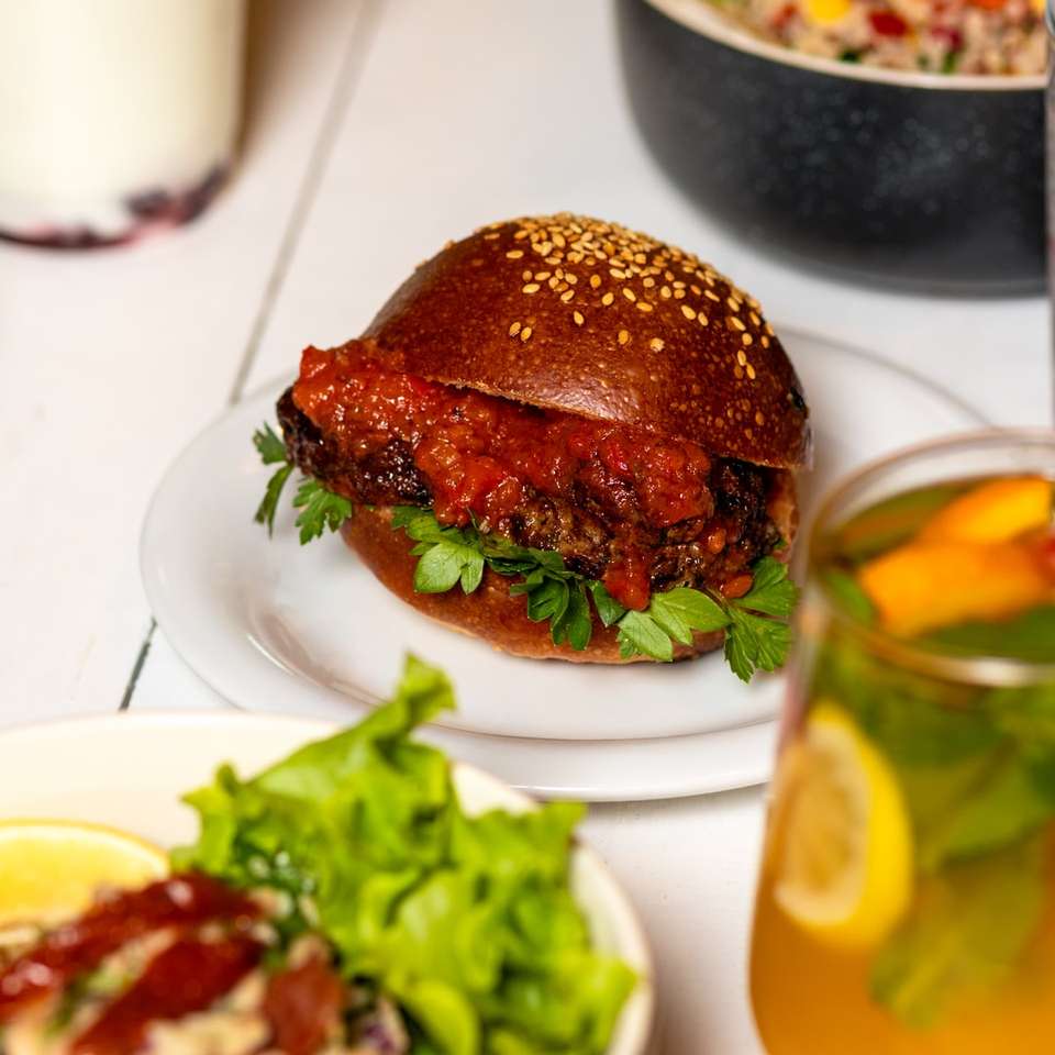 hamburger sul piatto in ceramica bianca accanto a un bicchiere trasparente puzzle online
