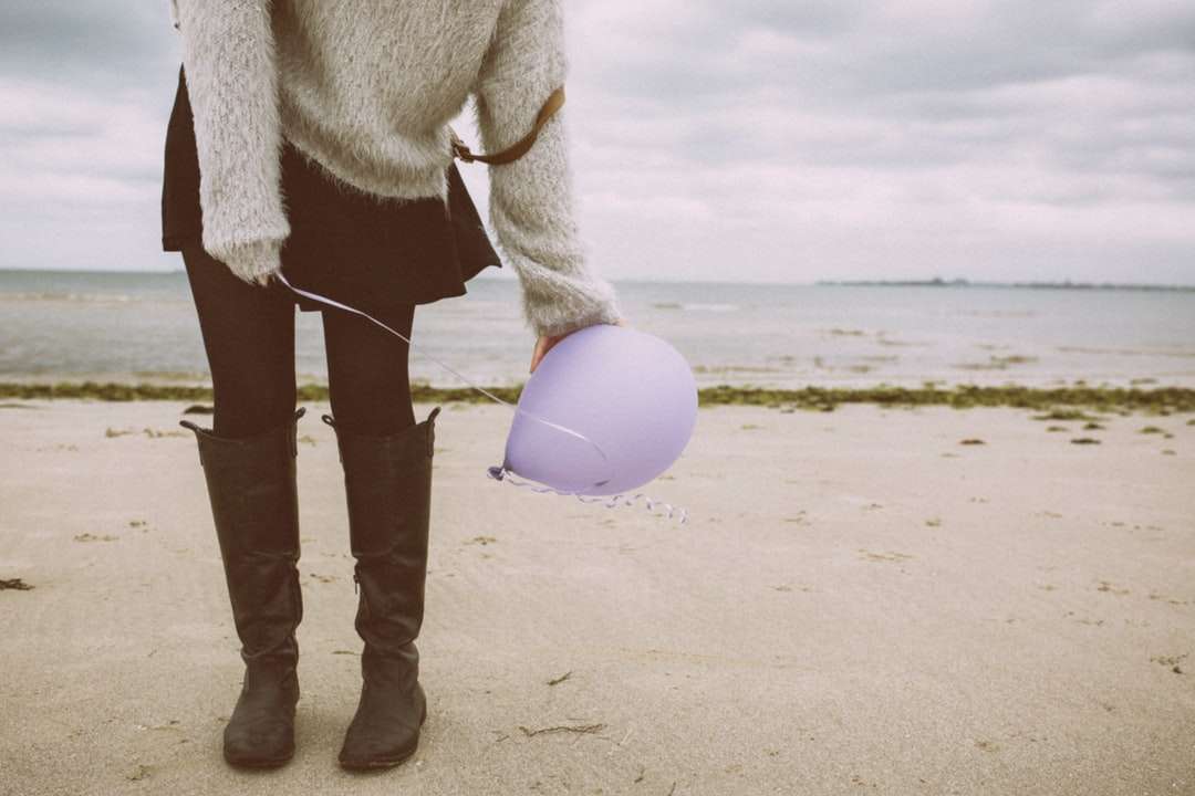 vrouw in grijze bontjas en zwarte broek staande op het strand online puzzel