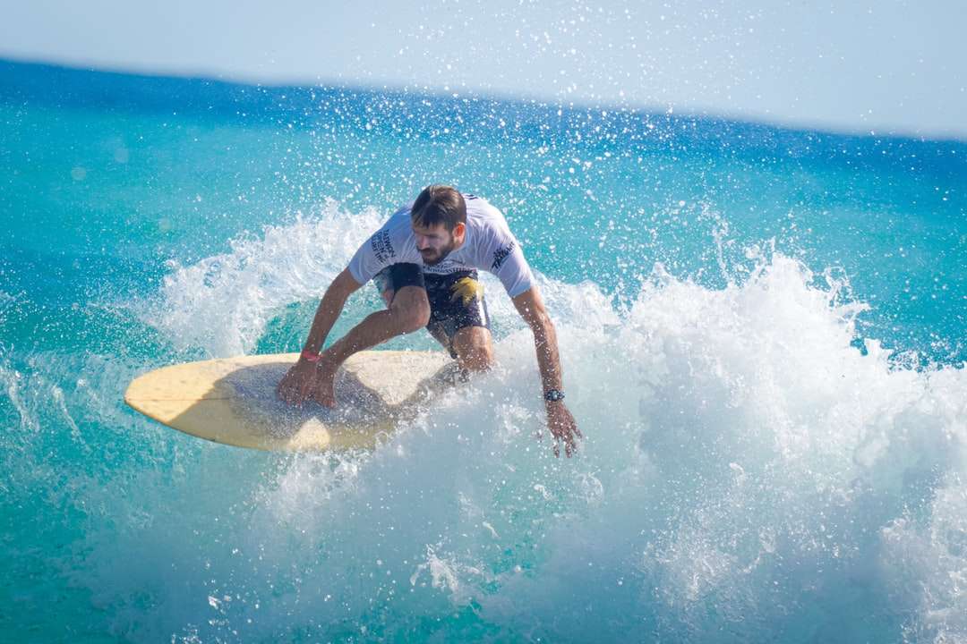 Hombre de camiseta blanca y pantalones cortos azules surfeando en las olas del mar rompecabezas en línea
