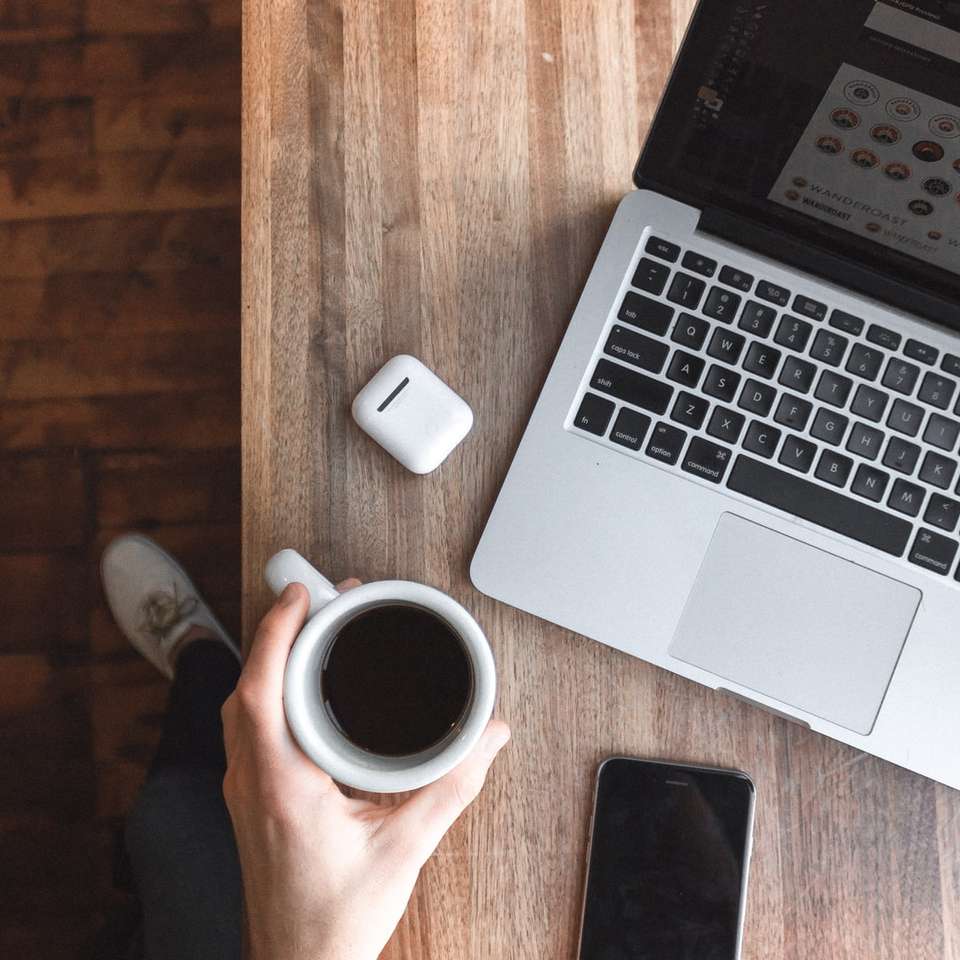 Persona sosteniendo una taza de café junto a la computadora portátil gris rompecabezas en línea