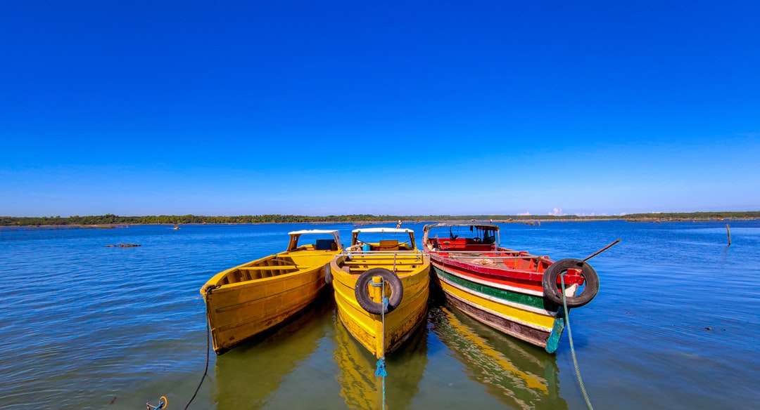 röd och gul båt på vatten under blå himmel under dagtid Pussel online