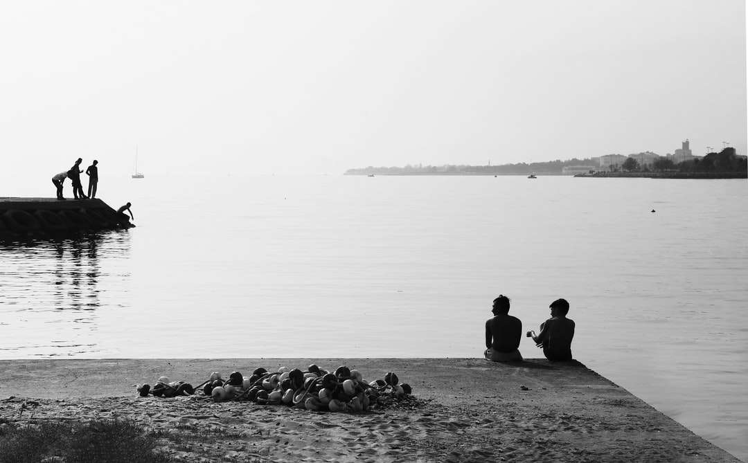 silhouette de gens assis sur un rocher près du plan d'eau puzzle en ligne