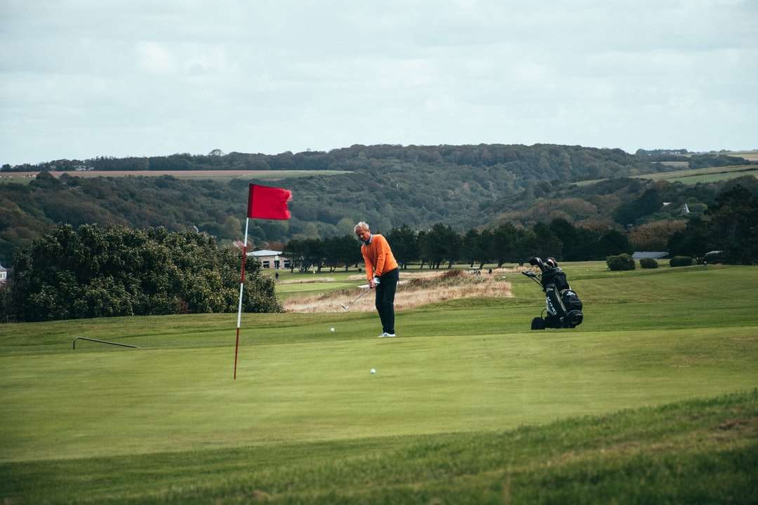 мужчина в оранжевой куртке и черных штанах держит клюшку для гольфа пазл онлайн