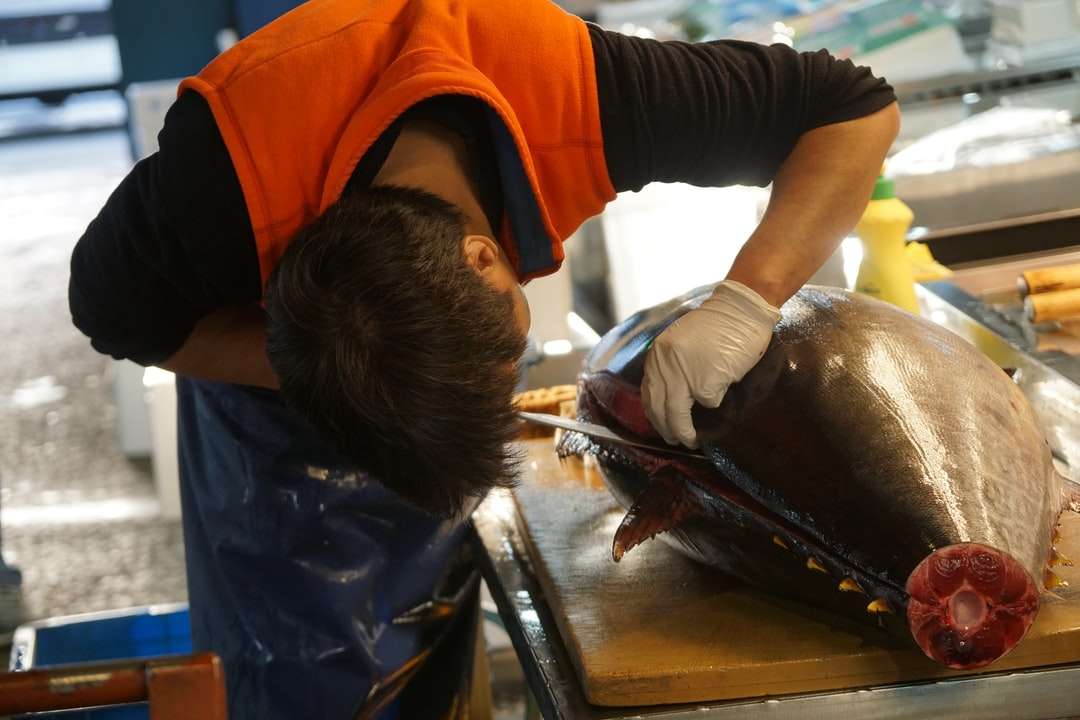 homem de camiseta laranja e calça preta segurando um peixe preto quebra-cabeças online