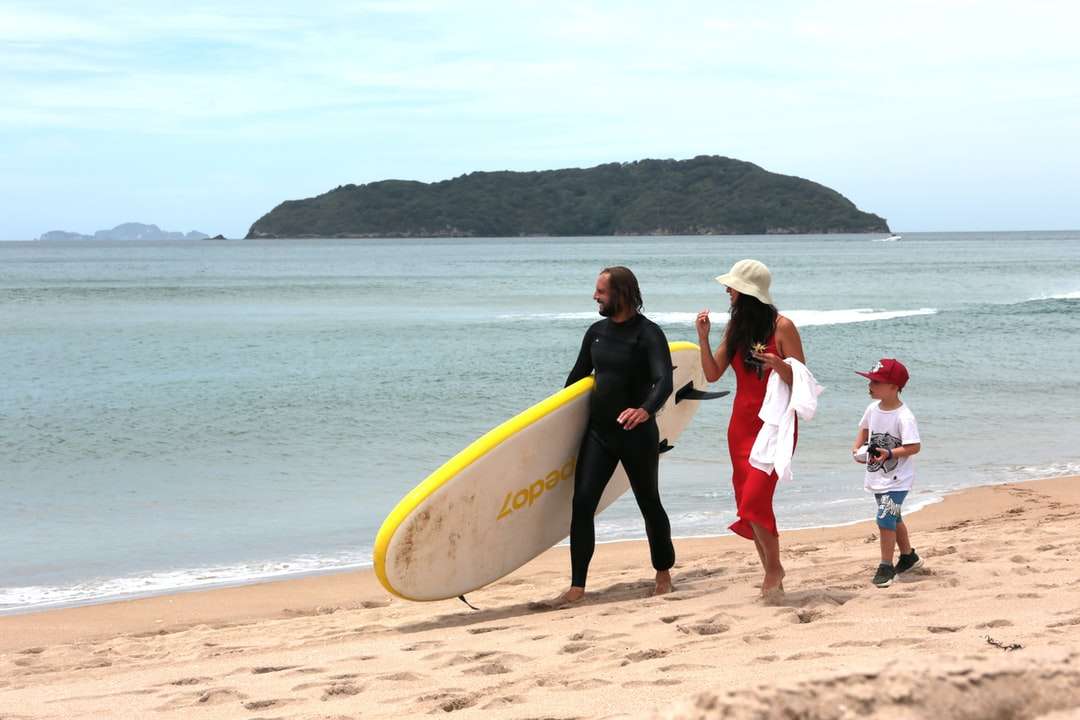 bărbat și femeie ținând o placă de surf galbenă mergând pe plajă puzzle online