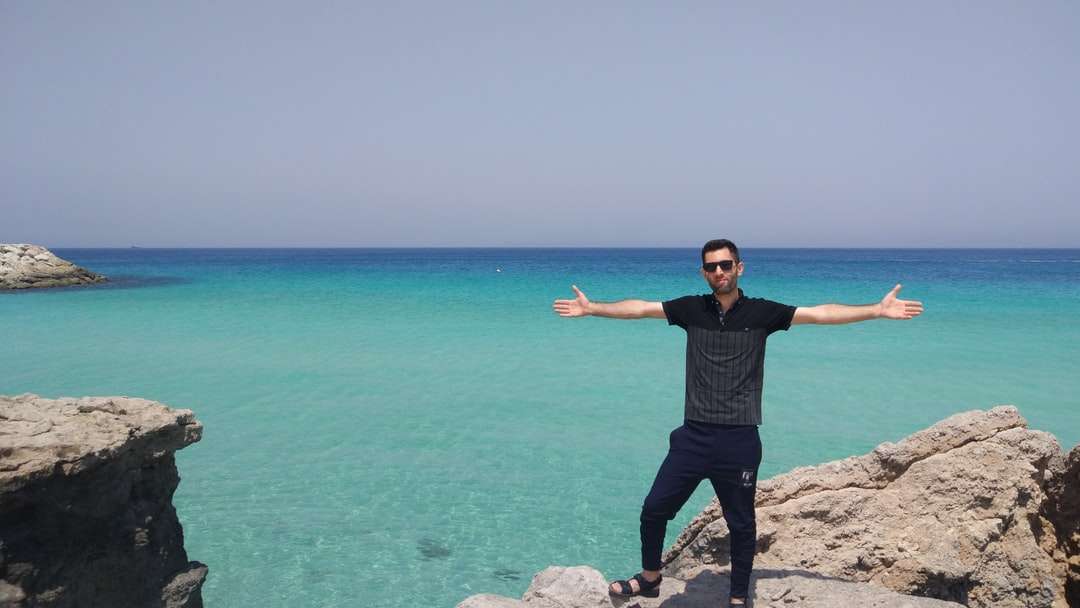 man in zwart t-shirt staande op rots in de buurt van zee online puzzel