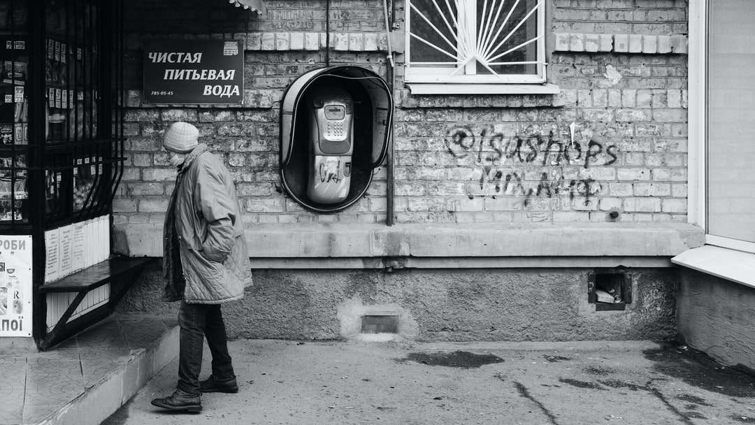 Hombre de chaqueta gris de pie cerca de la pared con graffiti rompecabezas en línea