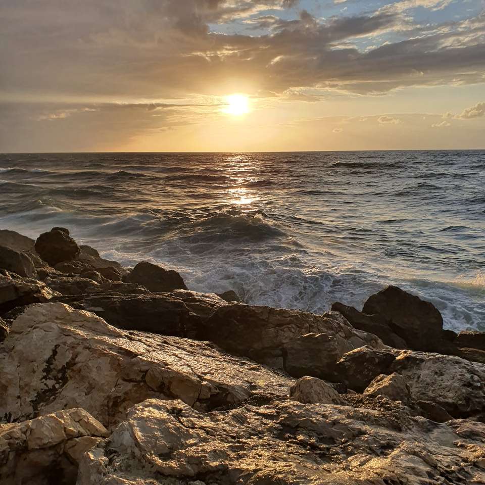 szürke sziklás parton naplemente alatt online puzzle