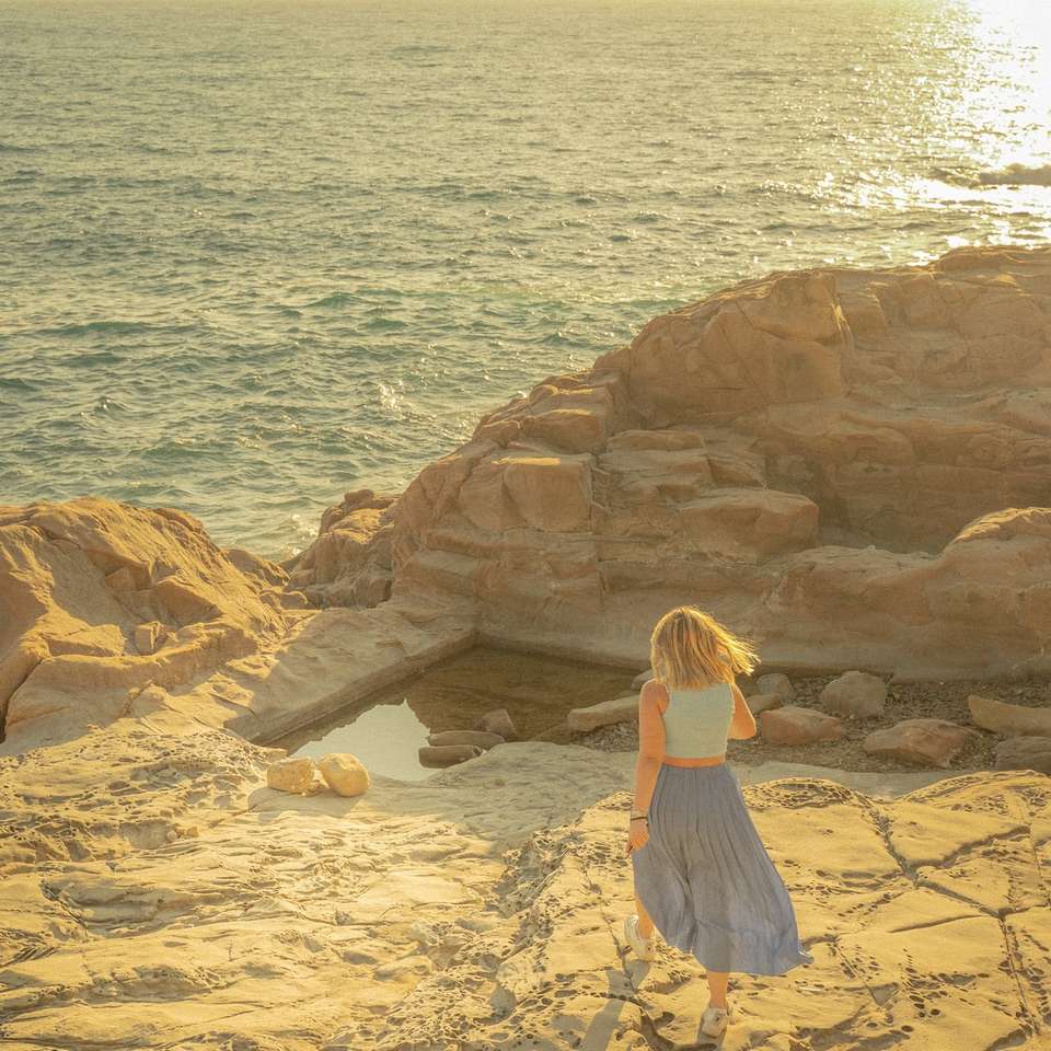 Frau im weißen Kleid sitzt auf braunem Felsen nahe Körper Online-Puzzle