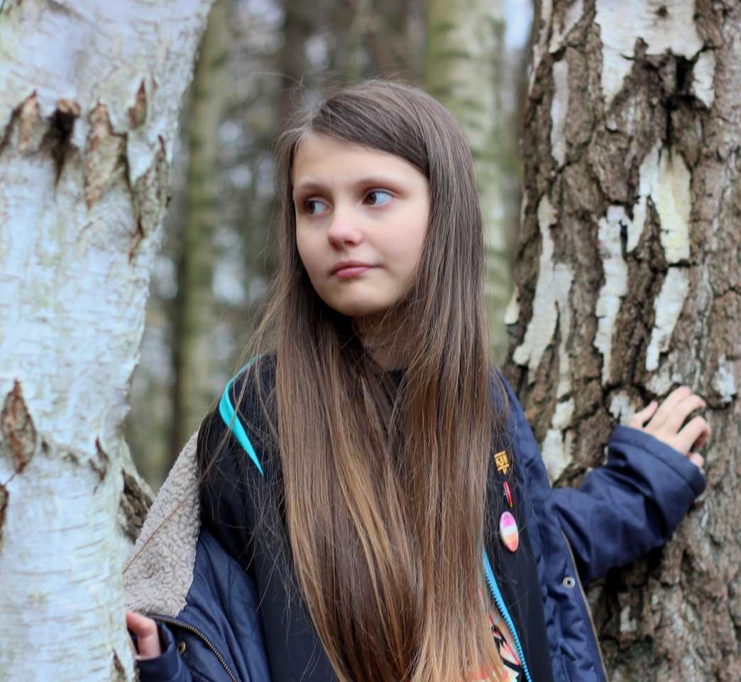 Frau in schwarzer Jacke, die sich auf braunen Baum stützt Online-Puzzle